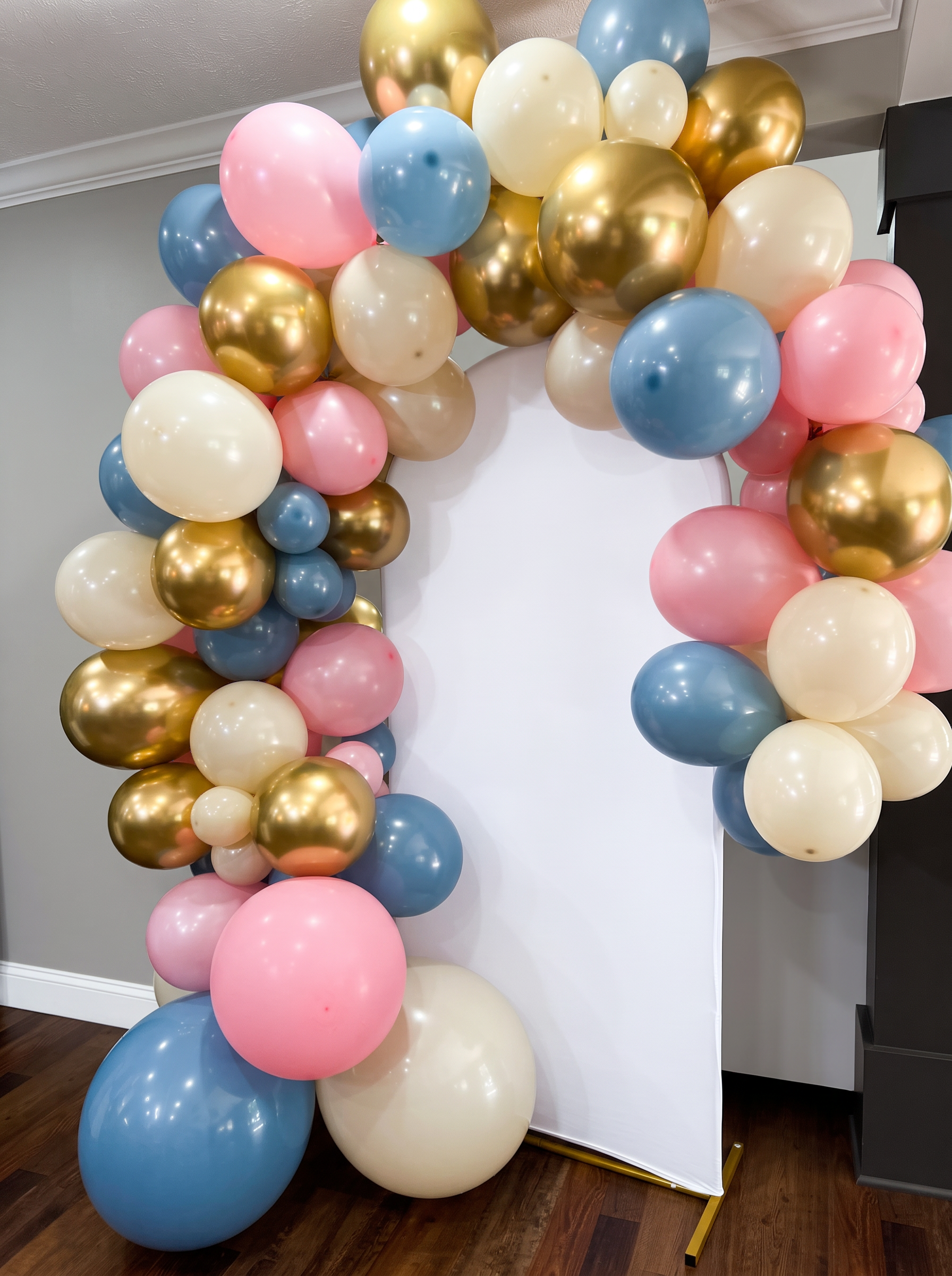 Pink, dusty blue, gold and cream balloon arch around a white backdrop