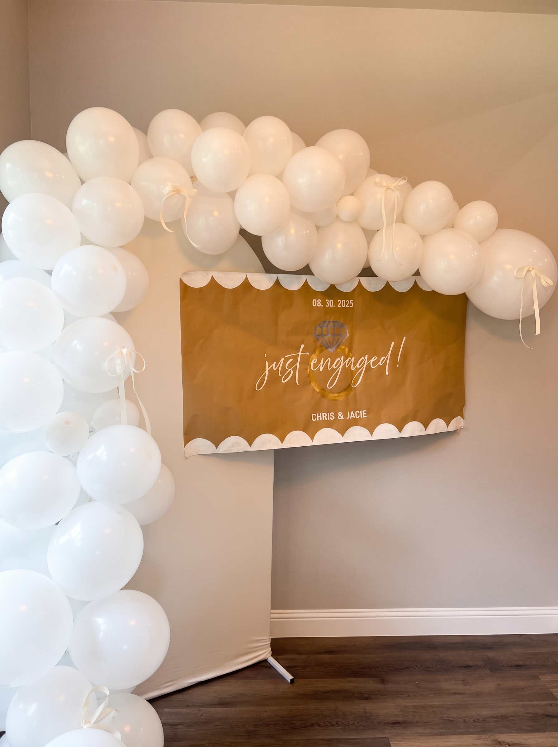 White balloon garland above a gold just engaged sign